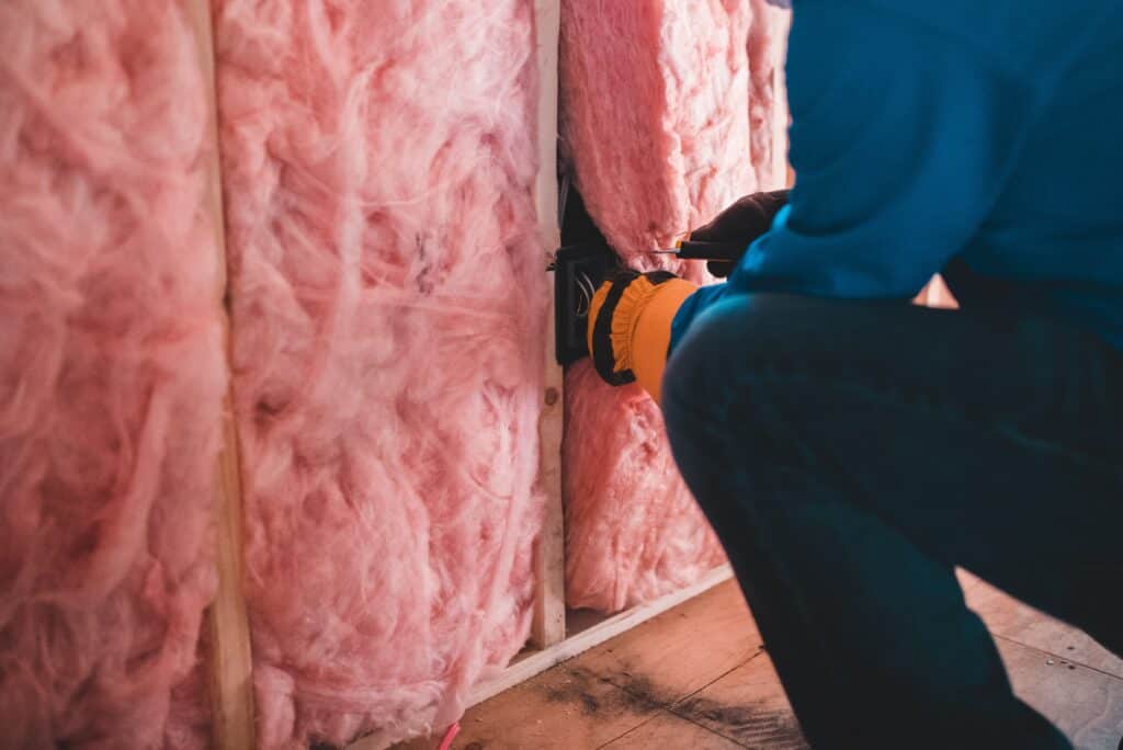 person installing pink insulation between the studs in a home