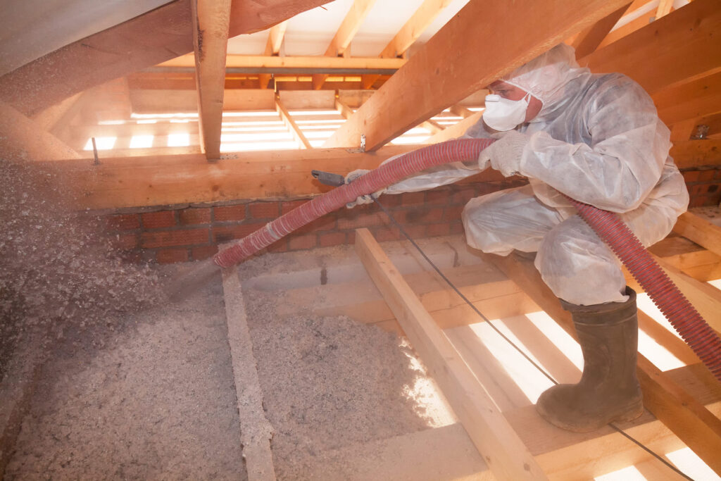 A Man Is Spraying Ecowool Insulation In The Attic Of