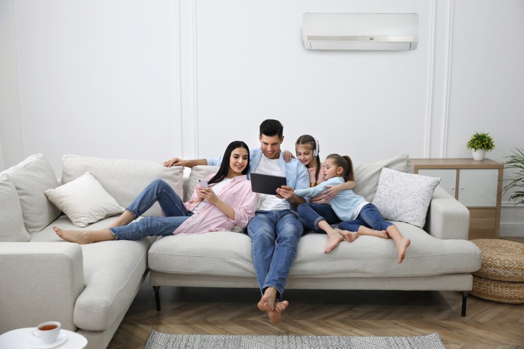 Happy Family Resting Under Air Conditioner On White Wall At