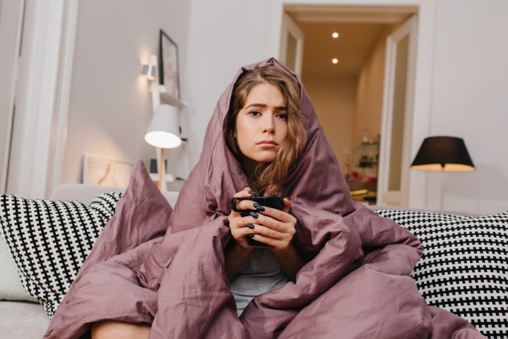 Grumpy woman under a blanket holding a mug